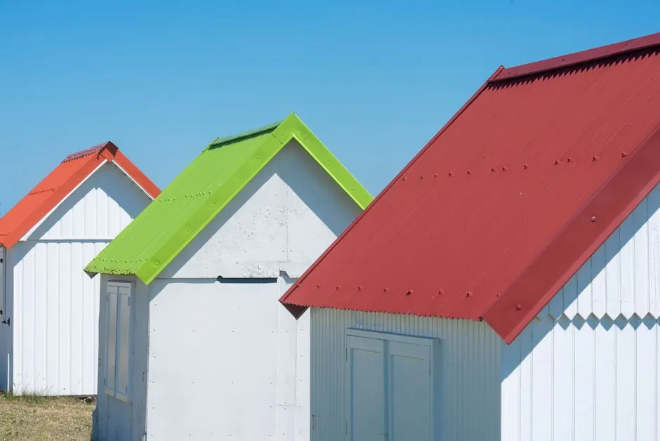 White beach huts with bright red, green, and orange rooftops under a clear blue sky.